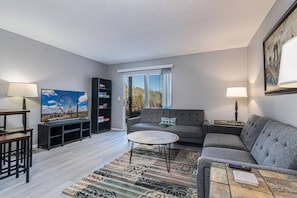 A living room with a sofa, coffee table, TV, bookshelf, and a window with a view. - The "Merlot" - Updated Condo - DISCOUNT 4+ nights! (Branson)