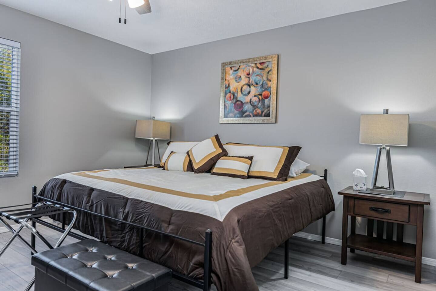 A modern bedroom with a large bed, bedside tables, a bench, and a painting on the wall.