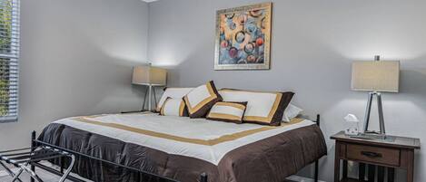 A modern bedroom with a large bed, bedside tables, a bench, and a painting on the wall.