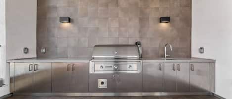 A modern kitchen with stainless steel cabinets, a built-in grill, and two wall-mounted lights.