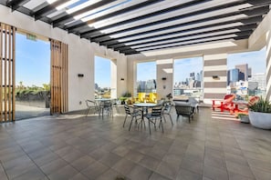 A rooftop terrace with a city skyline view, featuring outdoor seating and potted plants.