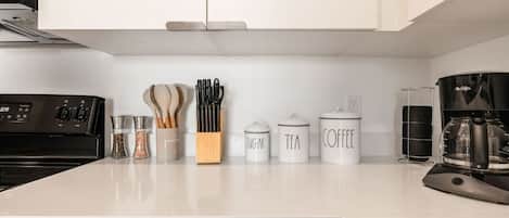 A kitchen with a stove, coffee maker, and labeled containers for sugar, tea, and coffee.