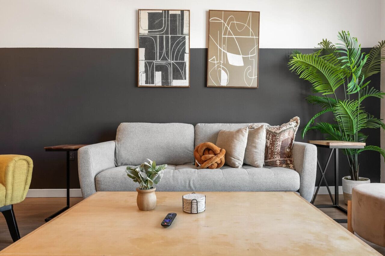 A living room with a grey sofa, a coffee table, a remote control, and two framed abstract artworks on the wall.
