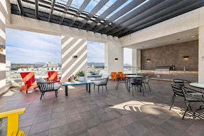 A rooftop patio with outdoor seating, a grill, and a view of the cityscape.