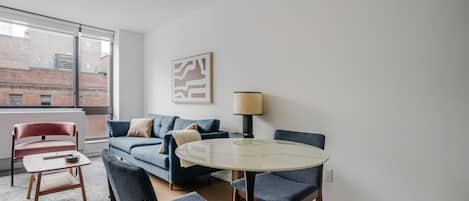 Ein modernes Wohnzimmer mit einer Couch, Sesseln, einem runden Tisch, einer Lampe und einem großen Fenster.