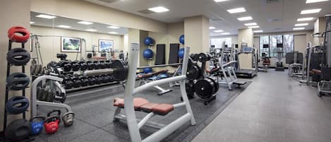 Ein Fitnessraum mit verschiedenen Trainingsgeräten, darunter Kurzhanteln, Kettlebells und Kraftmaschinen.