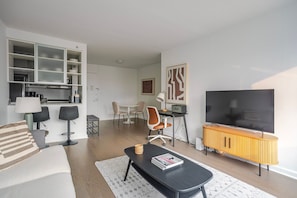 A modern living room with a sofa, a coffee table, a TV, a dining area with chairs, and a kitchen area with cabinets. - Blueground | Hell's Kitchen, fitness center, nr Central Park (New York)