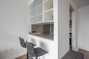 A modern kitchen with a built-in sink, two bar stools, and a glass-fronted upper cabinet. - Blueground | Hell's Kitchen, fitness center, nr Central Park (New York)