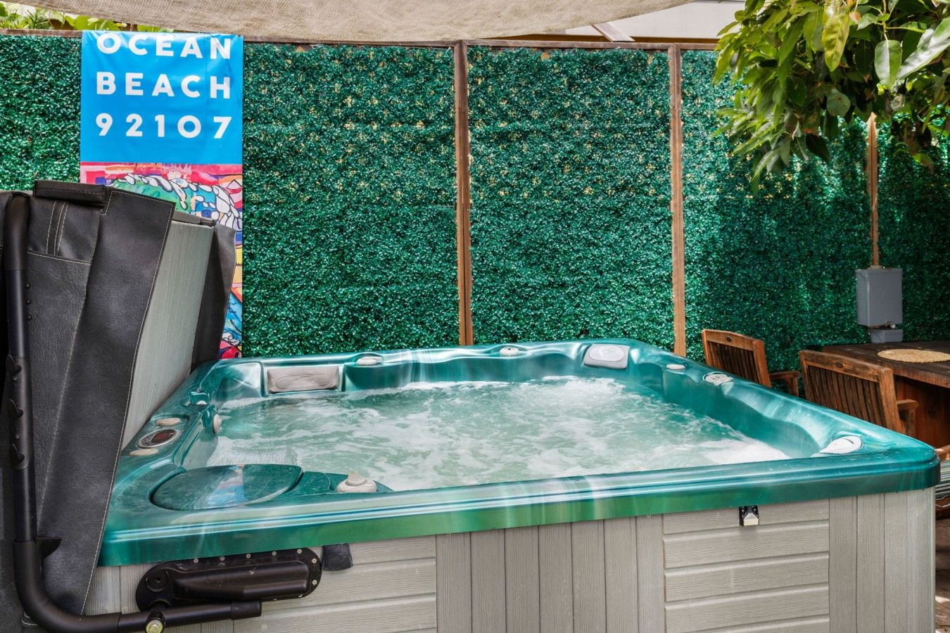 Un jacuzzi con estructura de madera y cubierta verde, frente a una pared verde con un letrero que dice 'OCEAN BEACH 92107'.