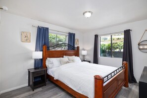 A bedroom with a wooden bed, two bedside tables, a nightstand, a window with curtains, and a ceiling light. - Avocado Hut- HOT TUB, free parking (San Diego)