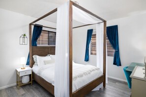 A four-poster bed with white bedding, a bedside table with a lamp, and a nightstand with a plant. - Avocado Hut- HOT TUB, free parking (San Diego)
