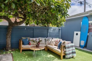 A cozy outdoor seating area with a wooden bench and cushions, surrounded by a blue fence and a tree. - Avocado Hut- HOT TUB, free parking (San Diego)