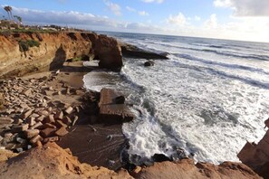 A rocky coastline with waves crashing onto the shore, a cliff with vegetation, and a clear sky. - Avocado Hut- HOT TUB, free parking (San Diego)