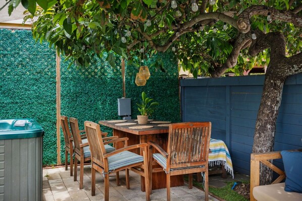 An outdoor patio area with a wooden table and chairs, a hot tub, and a green wall backdrop. - Avocado Hut- HOT TUB, free parking (San Diego)