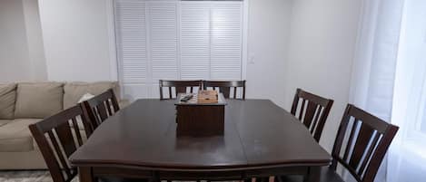 A dining area with a rectangular table, six chairs, and a window with blinds.