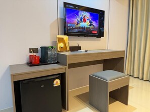 A hotel room with a TV mounted on the wall, a small refrigerator, a wooden desk, a cushioned bench, and a tray with a red mug and glasses. - Happy Room 3 (Pattaya)