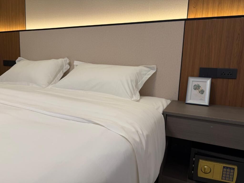 A hotel room with a bed, a nightstand, a safe, and a framed certificate on the nightstand.