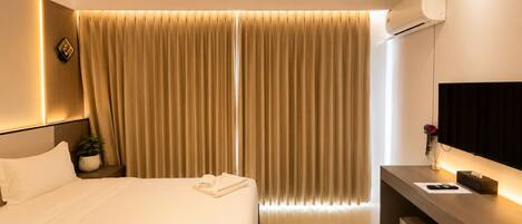 A hotel room with a bed, bedside table, TV, and curtains.