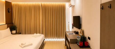 A hotel room with a bed, a desk, a mirror, a TV, and a wardrobe.