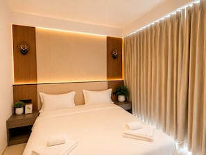 A hotel room with a large bed, two bedside tables, a nightstand, a potted plant, and a window with curtains. - Happy Room 3 (Pattaya)