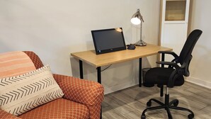 Een kamer met een houten bureau, een zwarte bureaustoel, een oranje sofa met patroon en een witte deur met een ruit.