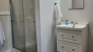 Een badkamer met een glazen douchecabine, een wit wastafelmeubel met lades, een spiegel en een lamp boven de spiegel.