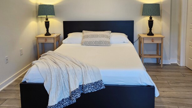 Een slaapkamer met een groot bed, twee nachtkastjes met lampen, een houten vloer en een plafond met inbouwverlichting.