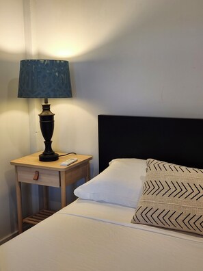 A neatly made bed with white linens and patterned pillows, a bedside table with a lamp, and a remote control. - Quiet 1-bedroom apartment in charming Elloree, SC (Elloree)