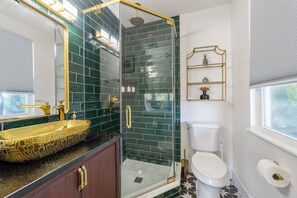Ein Badezimmer mit einer Duschkabine, einem goldenen Waschbecken und einem WC mit weißem Tank.