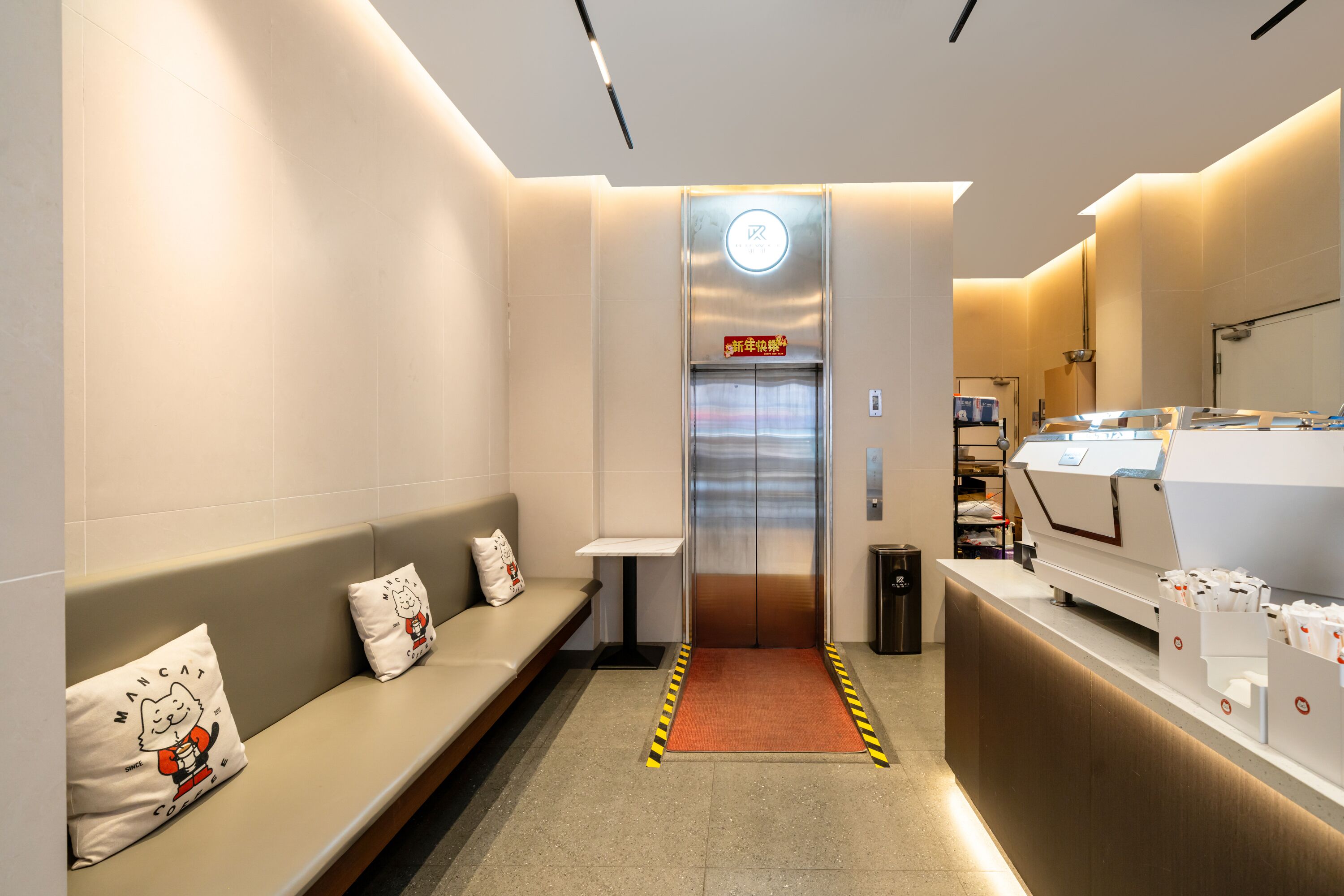 Um elevador moderno com painel digital, área de estar com almofadas e máquina de café.