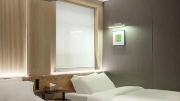 A hotel room with a bed, bedside table, and a window with blinds.