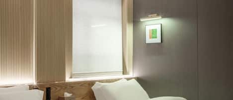 A hotel room with a bed, bedside table, and a window with blinds.