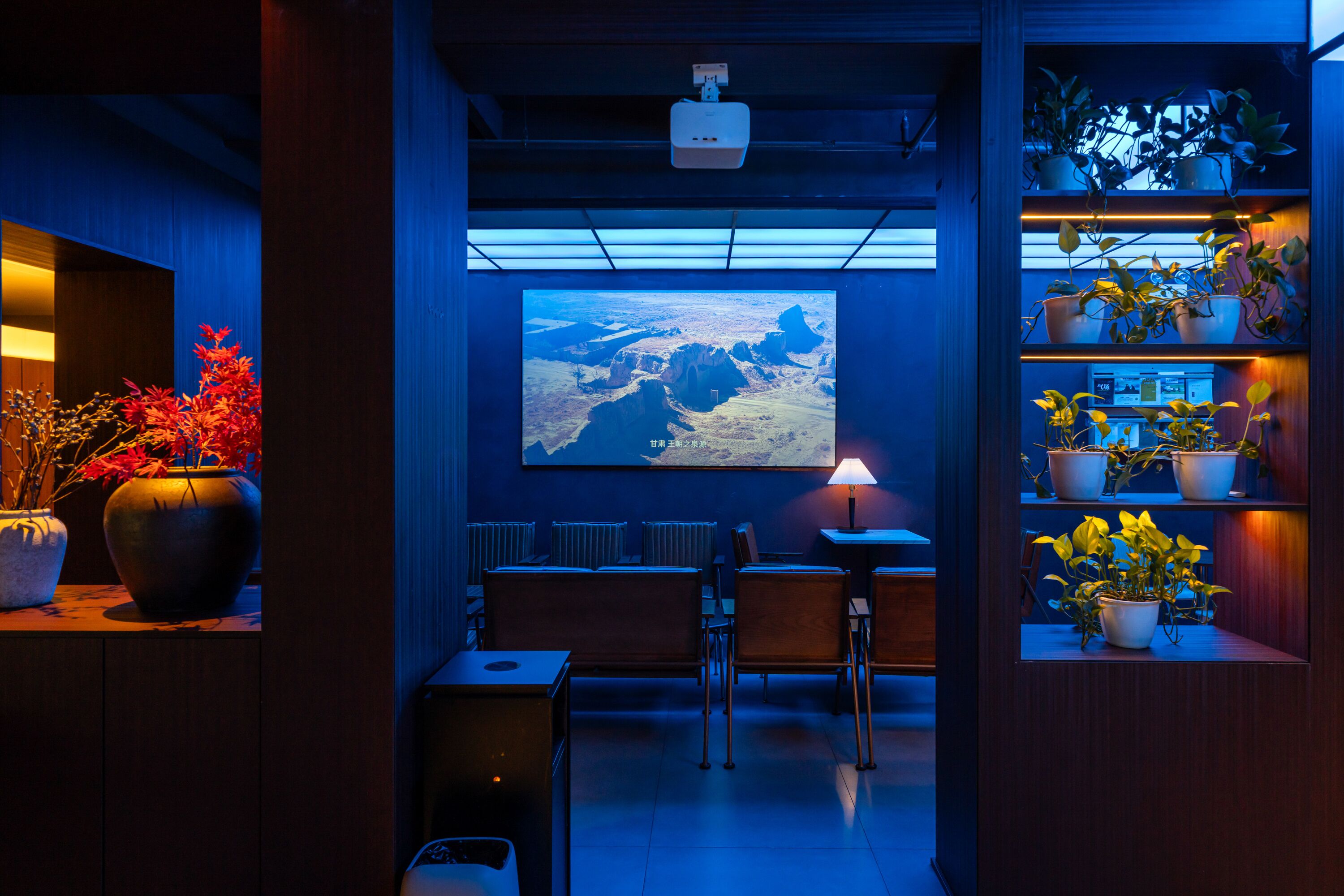 A conference room with a large screen displaying a landscape, wooden furniture, and potted plants.