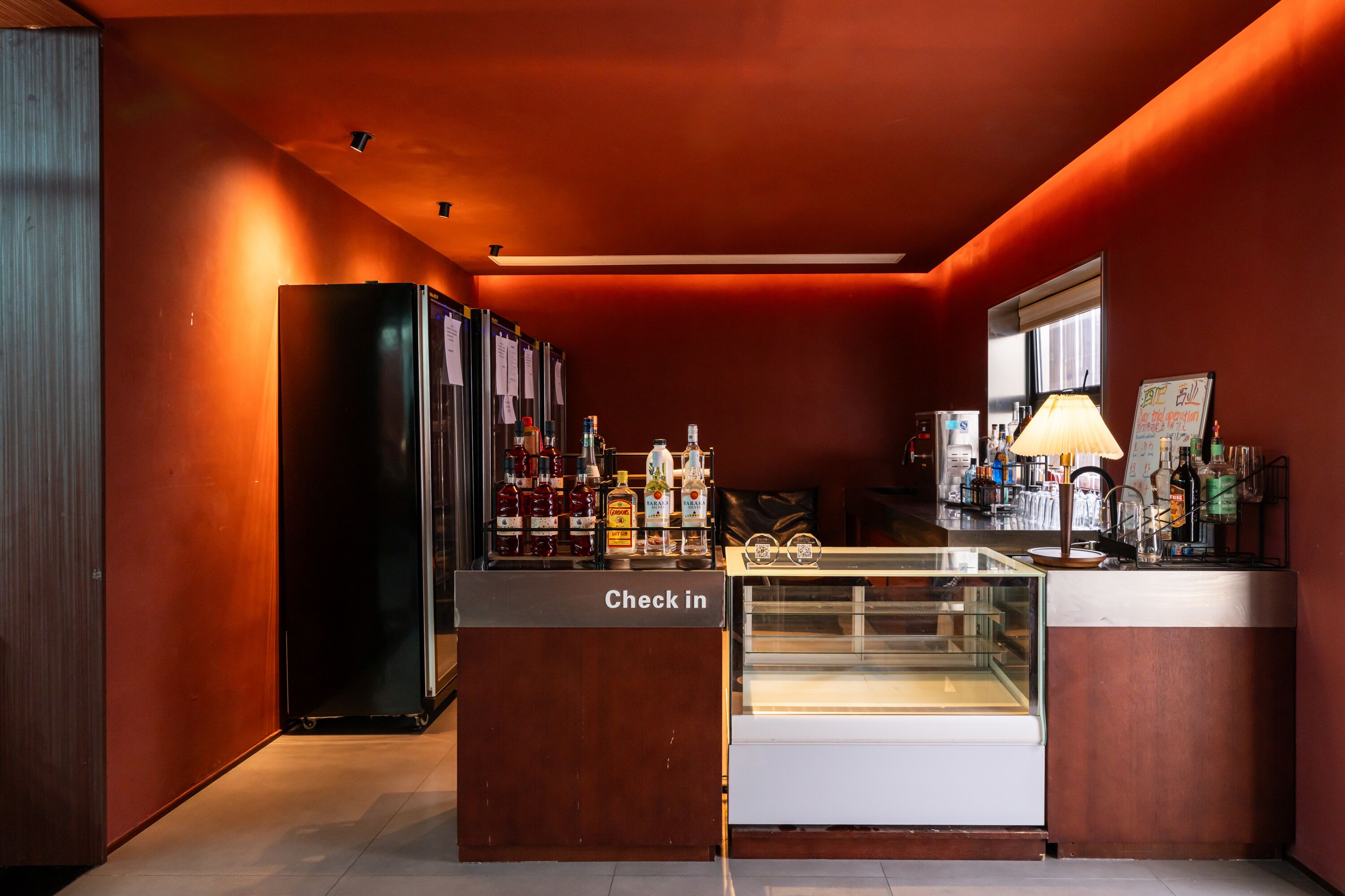 Una zona de bar con una recepción, estantes llenos de botellas de licor y una vitrina de cristal.