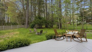 Eine Terrasse mit Gartenmöbeln, einem Feuerkorb und einem Holzzaun in einer bewaldeten Gegend.