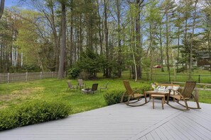 Eine Terrasse mit Gartenmöbeln, einem Feuerkorb und einem Holzzaun in einer bewaldeten Gegend.