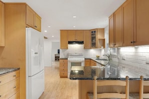 A kitchen with wooden cabinets, a white refrigerator, a stove, and a granite countertop. - Charming 3-bedroom house in peaceful Scarborough perfect for relaxing. (Scarborough)