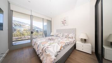 A bedroom with a large bed, a nightstand, a lamp, and a view of a building through a glass door.
