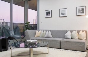 A modern living room with a grey sofa, black chairs, a glass coffee table, and framed pictures on the wall. - Modern Retreat near stadiums (Lidcombe)