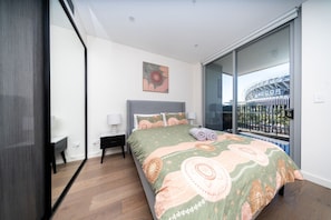 A bedroom with a bed, bedside tables, a window with a view of a stadium, and a painting on the wall.
