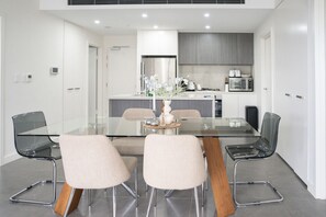 A modern dining area with a glass table, four chairs, and a central vase with flowers.