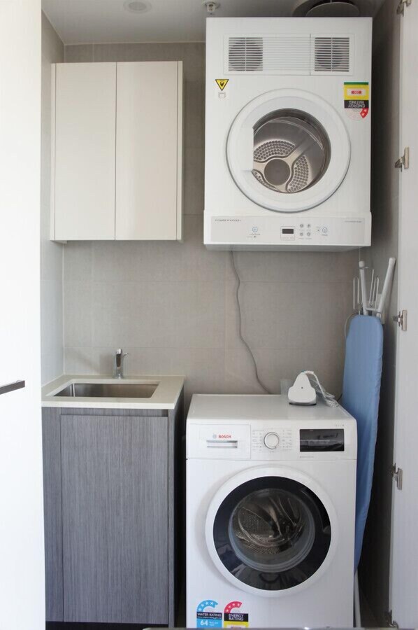 A compact laundry room with a Bosch washing machine and dryer, a sink, and cabinets.