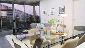 Ein modernes Wohnzimmer mit Glastisch, grauem Sofa und Blick auf eine Brücke durch große Fenster.