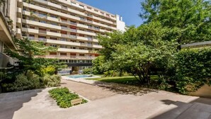 Un edifici d'apartaments de diverses plantes amb un pati que compta amb una piscina, vegetació i una zona de jardí.