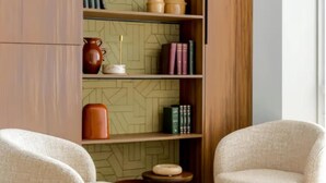 Una habitació amb una biblioteca, dos seients còmodes, una petita taula auxiliar i un mur amb un disseny decoratiu.