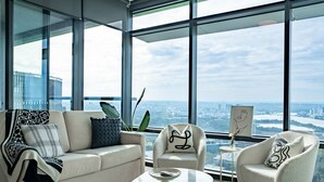 A modern living room with a sofa, armchair, and coffee table, large windows with a city view. - Sydney Olympic Park View Bliss | Modern Design (Sydney Olympic Park)