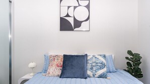 A bedroom with a bed, pillows, a nightstand, a lamp, and a wall art piece. - Sydney Olympic Park View Bliss | Modern Design (Sydney Olympic Park)