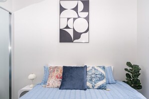 A bedroom with a bed, pillows, a nightstand, a lamp, and a wall art piece. - Sydney Olympic Park View Bliss | Modern Design (Sydney Olympic Park)