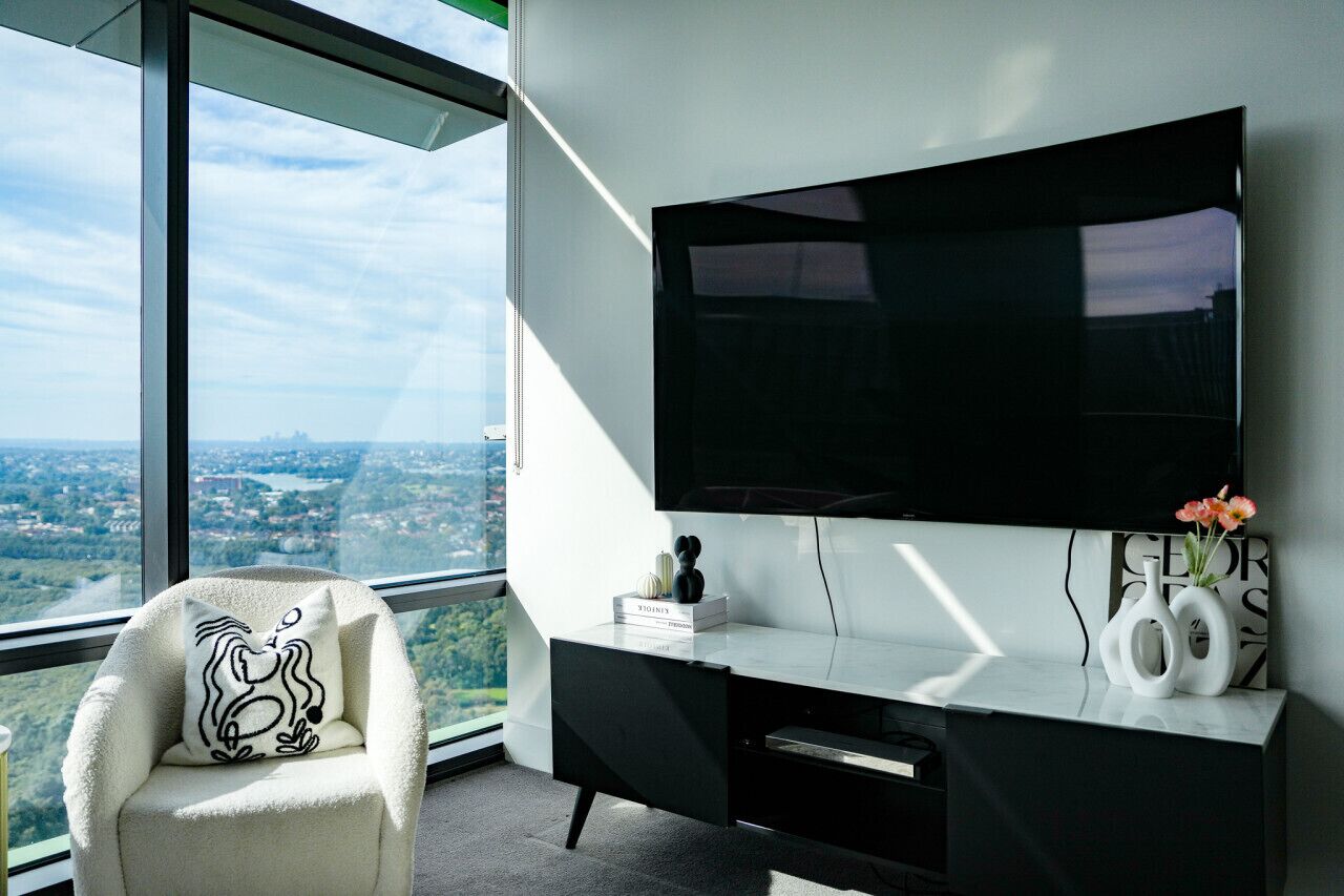 A modern room with a large TV, a comfortable chair, and a desk with a view of a cityscape.