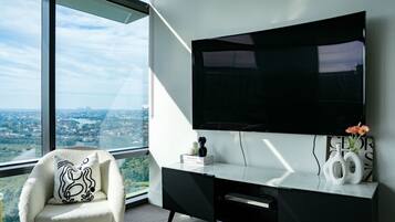 A modern room with a large TV, a comfortable chair, and a desk with a view of a cityscape.